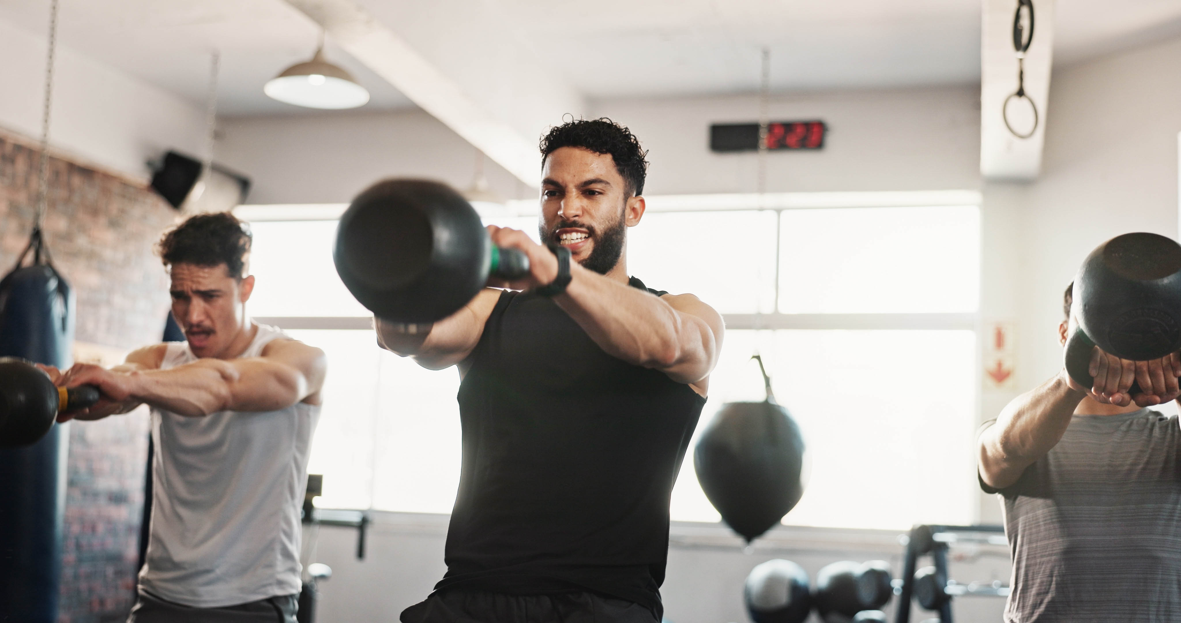 Three fit men doing kettlebell swings in a group workout at the gym